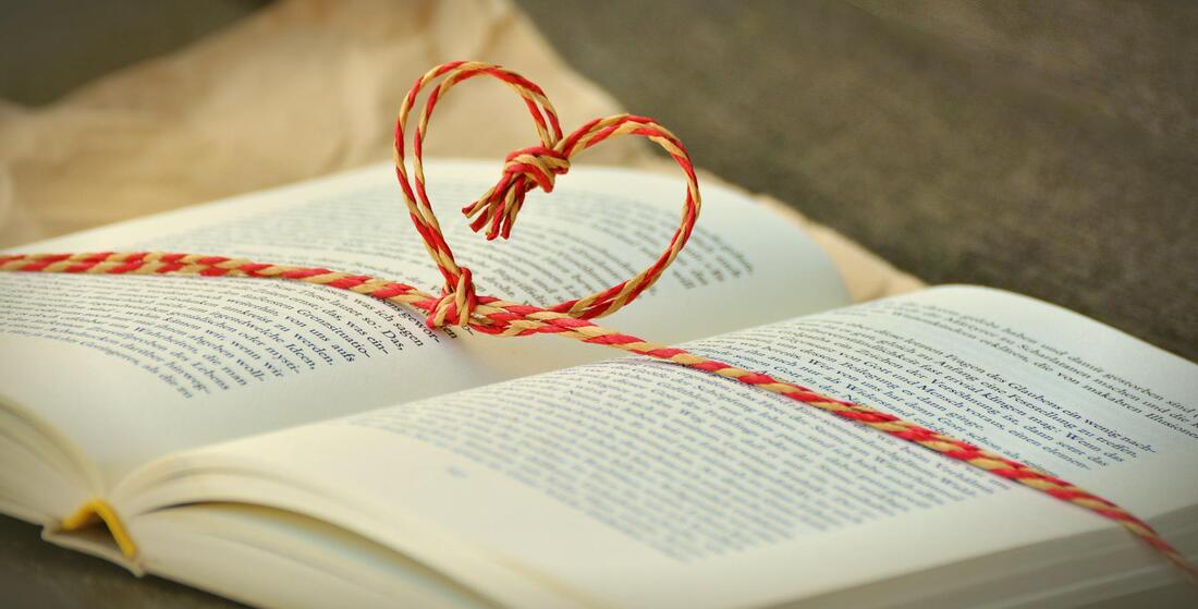 Book laying flat open with a red and yellow string laying across it, the center tied in a heart shape standing above the book