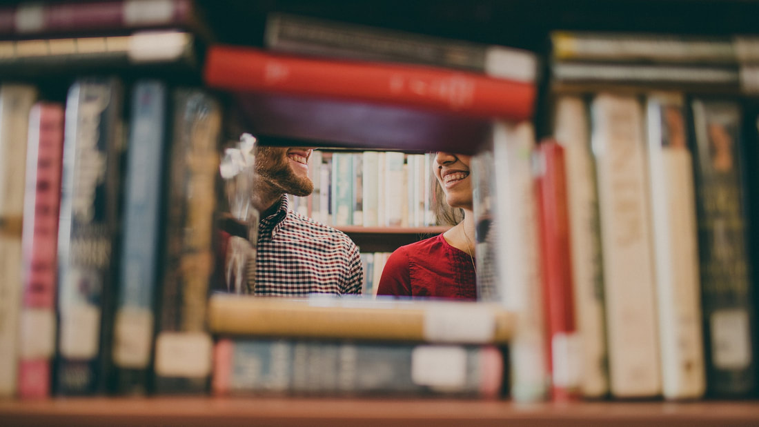 Looking through bookstacks at two people smiling at eachother