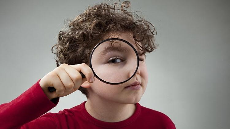 Young child holding a magnifying glass up to their face