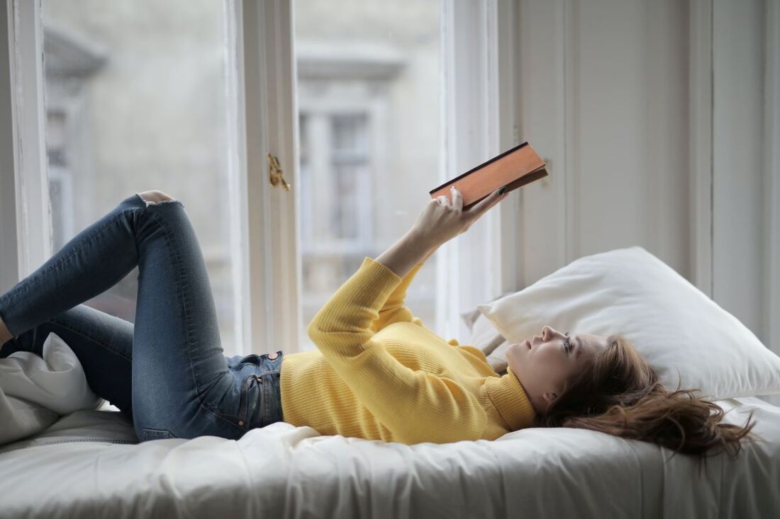 Woman lying on a bed holding a book above her as she reads.