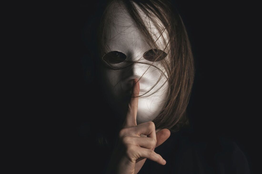 Masked person putting a finger over their lips to signal quiet